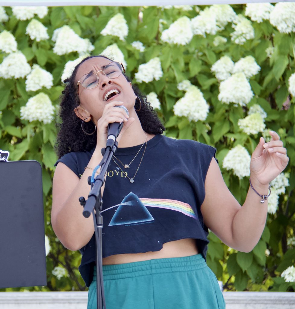 sabrina genesis singing in front of flowers with eyes closed