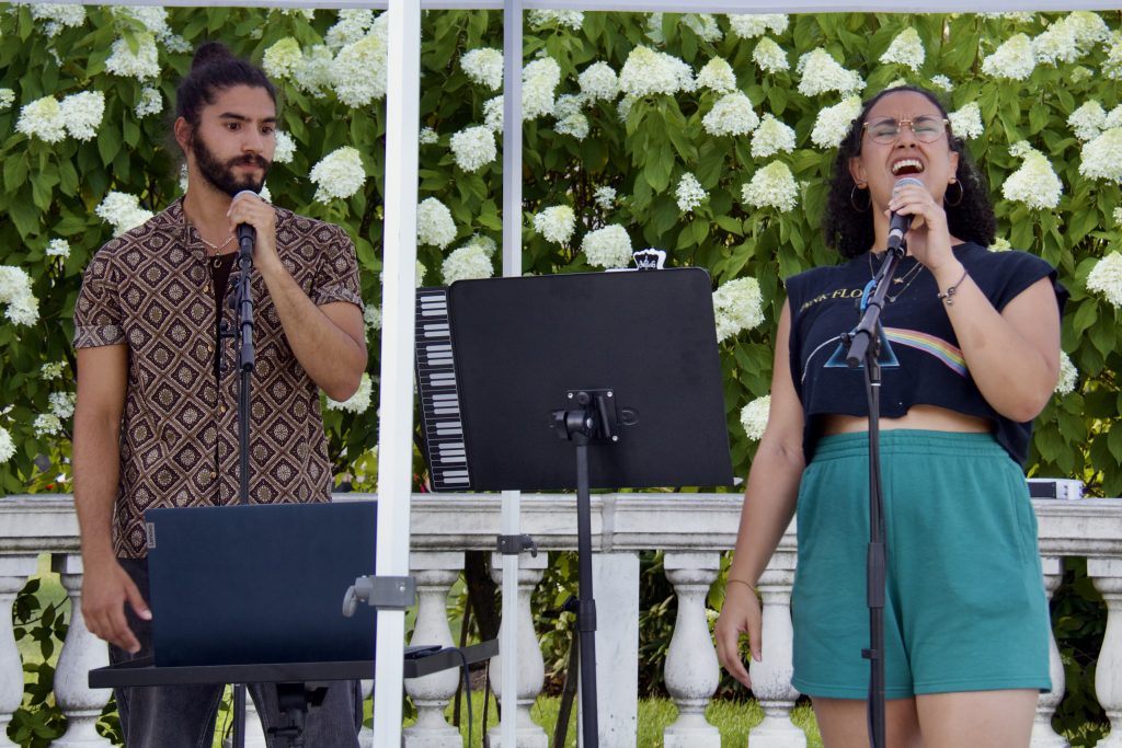 sabrina genesis singing in front of flowers with background singer