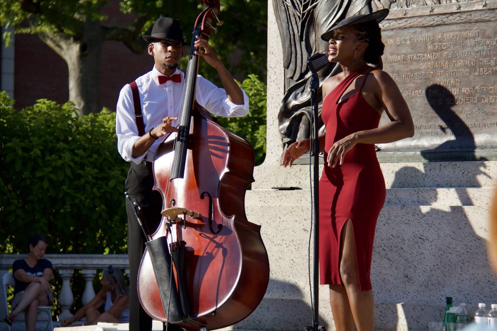 acute inflections, woman in red dress and hat singing with man in button down shirt playing cello